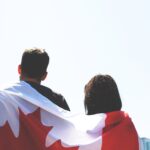Un drapeau du Canada sur le dos d'un couple de dos regardant la CN Tower de Toronto