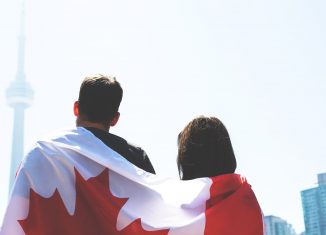Un drapeau du Canada sur le dos d'un couple de dos regardant la CN Tower de Toronto