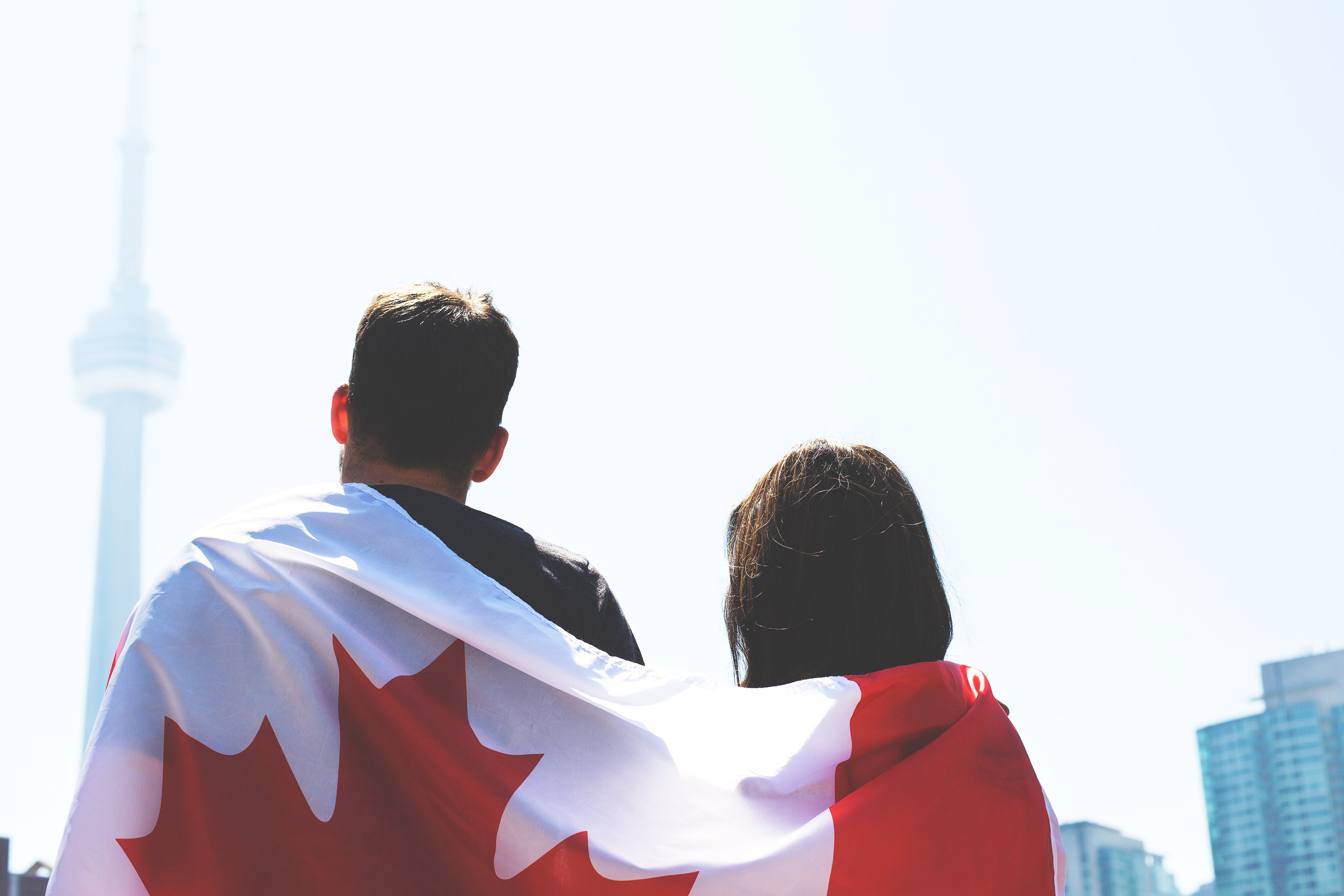 Un drapeau du Canada sur le dos d'un couple de dos regardant la CN Tower de Toronto